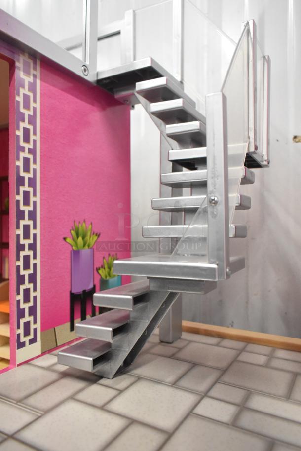 Doll playhouse with modern stairway, pink walls, and printed plant decor. Features silver railings and geometric patterns.