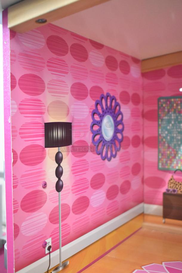 Doll playhouse interior with pink patterned walls, decorative mirror, floor lamp, and furniture, showcasing vibrant design.