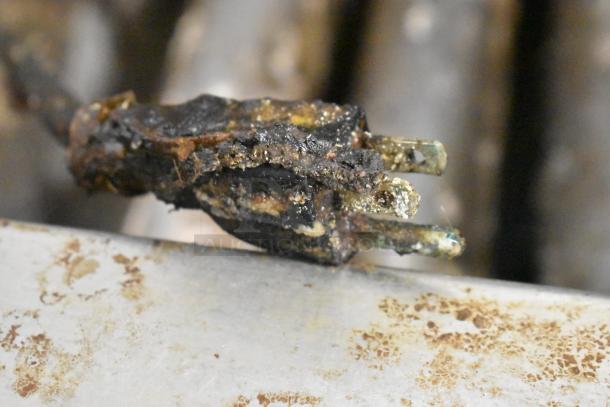 Burnt and corroded electrical plug with visible damage and grime buildup, indicating poor condition.