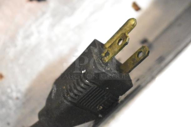 Close-up image of a black electrical plug with two brass prongs, showing signs of use and wear.