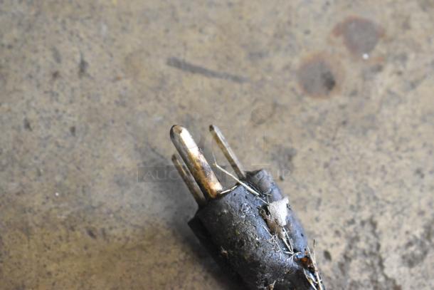 Close-up of a worn plug with exposed wires on a concrete floor. Dirt and debris are visible on the plug.