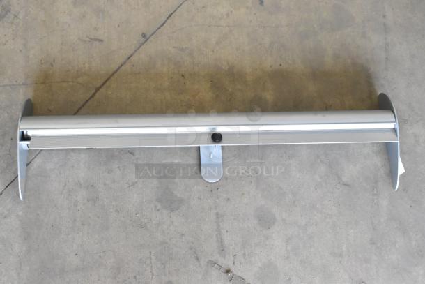 Silver roll-up sign base on concrete floor, in good condition, showing sturdy metal housing and support leg. No visible marks.