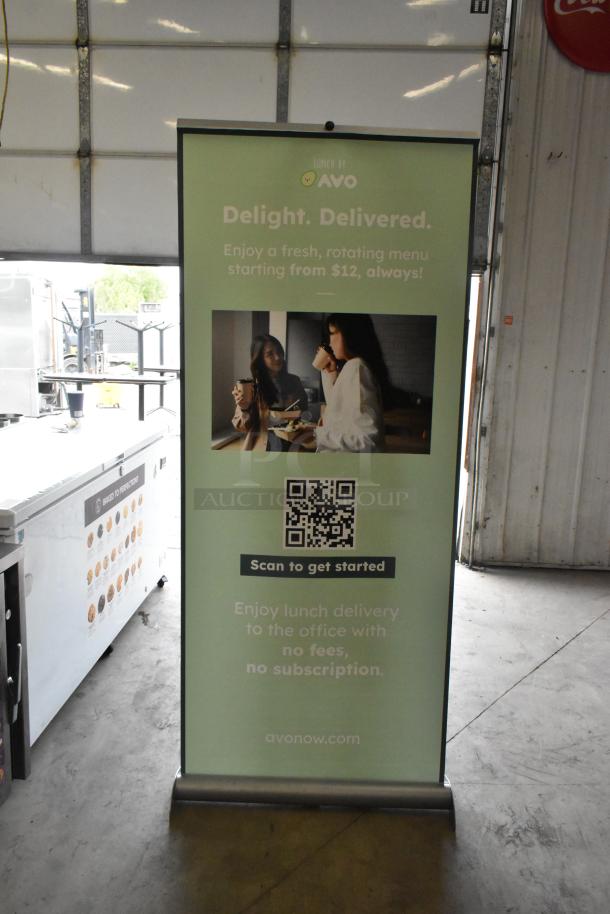 Roll-up sign for AVO, promoting lunch delivery services. Features QR code, imagery of two women, and details of a $12 menu.