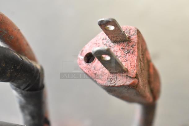 Close-up of a worn, 115-volt jigsaw plug with visible dirt, highlighting the cord's aged condition.