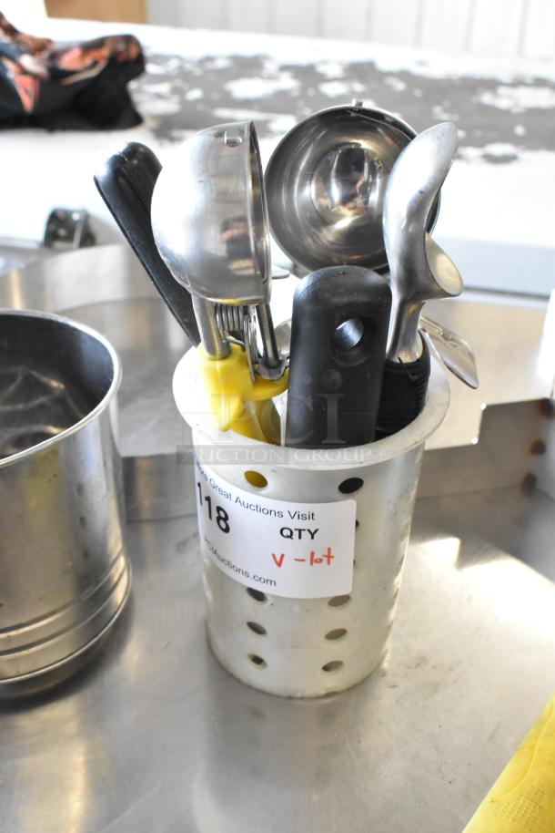 Lot of kitchen utensils in a perforated holder, including spatulas, scoops, and a paddle. Auction tag reads "QTY V-lot."