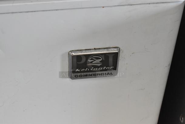 Kelvinator KCCF140WH metal chest freezer with hinge lid, visible "Kelvinator Commercial" logo. Slight surface wear.