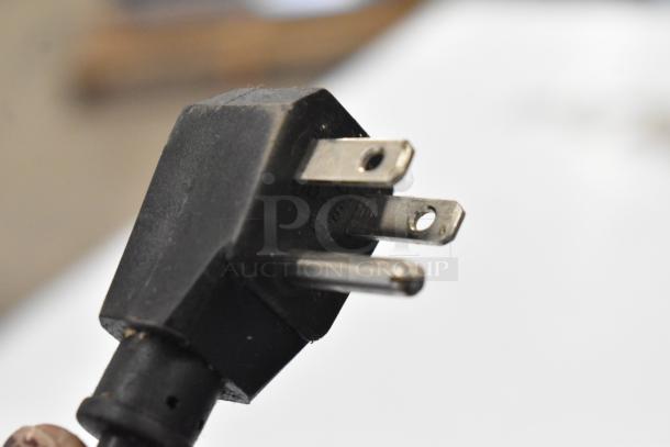 Close-up of a three-prong power plug, showing metallic prongs and a black housing. Suitable for 115 volts, 1 phase.