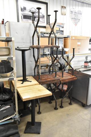 Eight tables with wooden tabletops, metal bases, and square feet, stacked for auction. Light and dark wood variations.