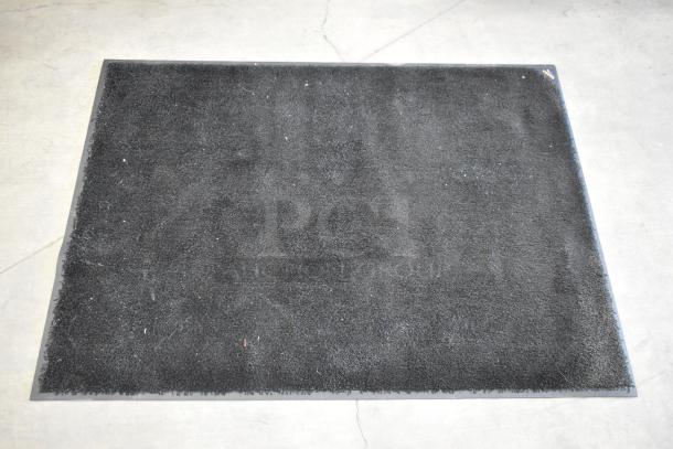 Black floor mat in used condition on a concrete surface.