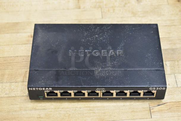 Netgear GS308 gigabit ethernet switch in used condition with eight ports shown on a wooden surface.