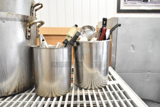 Lot of various kitchen items, including large stock pots, stainless steel bins with utensils, on industrial shelving.