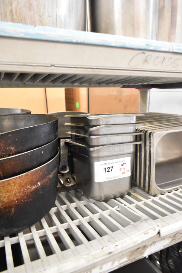 Lot of kitchen items on a shelf, including stock pots, stainless steel drop-in bins, and bowls. Auction label with "127 QTY" visible.
