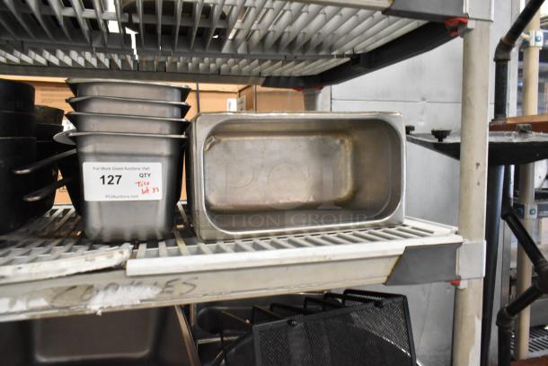 Lot of stainless steel stock pots, drop-in bins, and bowls on shelves. Includes label reading "127 QTY lot 33." Used condition.