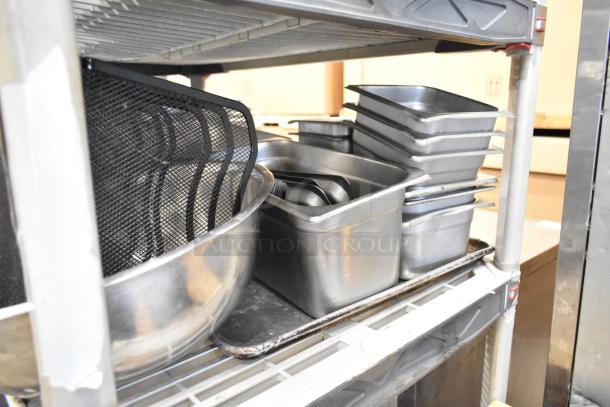 Lot of commercial kitchen items including stainless steel stock pots, drop-in bins, and bowls on metal shelving.