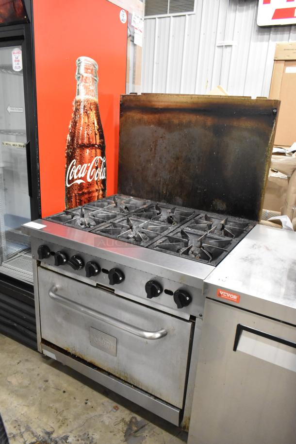 Mainstreet stainless steel 6-burner gas range with oven, over shelf, and backsplash. Used condition, visible wear.