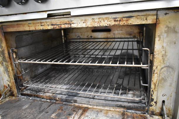 Mainstreet stainless steel commercial 6-burner gas range with oven, over shelf, and backsplash. Visible wear and stains.