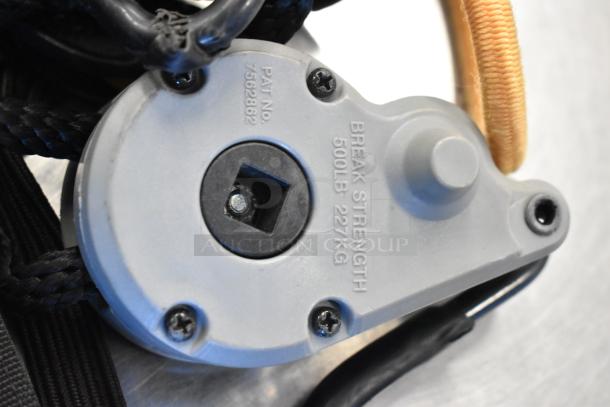 Close-up of a pulley mechanism with "BREAK STRENGTH 500LB 227KG" and patent number 7562862 visible, part of auction lot "4 Black Bags w/ Contents."