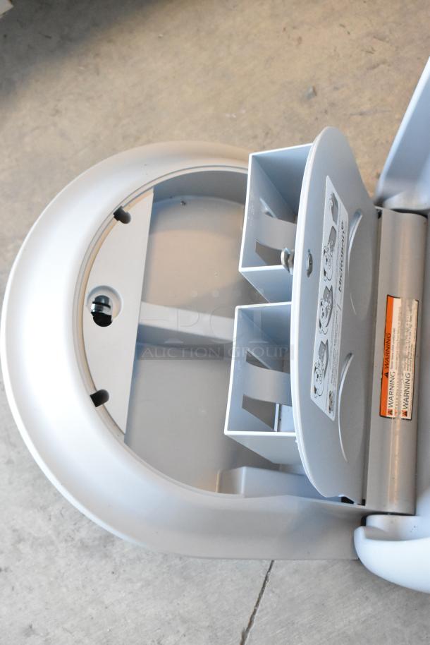 Koala Kare gray wall mount diaper changing station, open view, with safety straps and warning labels visible.