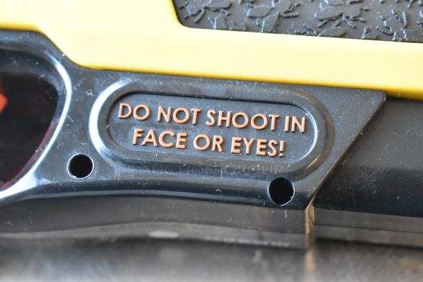 Warning label on a device: "DO NOT SHOOT IN FACE OR EYES!" Text in orange on a black surface.