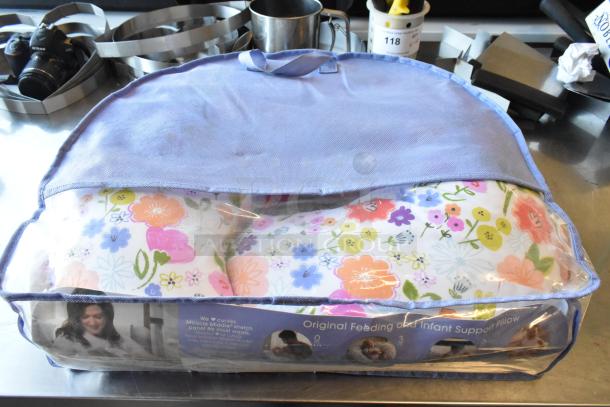Boppy Pillow in original packaging with floral design; suitable for feeding and infant support. Clear and blue bag.