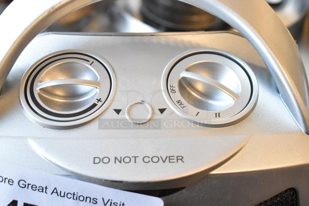 Close-up of a silver heater control panel with dials for temperature and settings, marked "DO NOT COVER."
