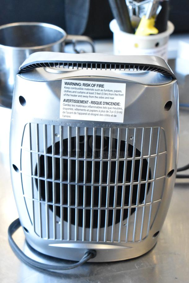 Metal heater with warning label about fire risk, visible grates, and power cord on a surface. Part of varied item auction lot.