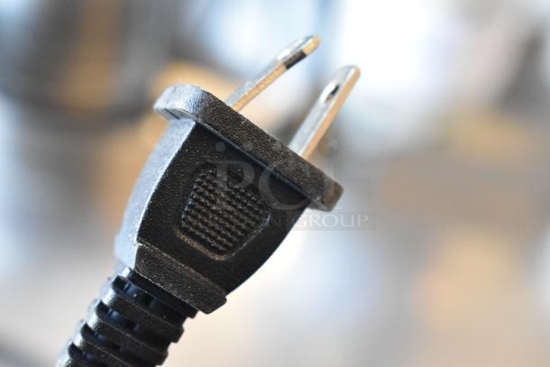 Close-up of a black electrical plug with two metal pins, part of a mixed auction lot.