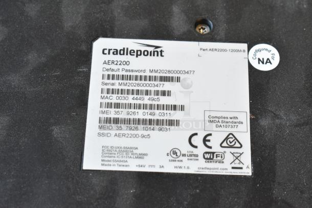 Cradlepoint AER2200 label showing part number, serial, MAC, IMEI, and compliance logos for a tech auction item.