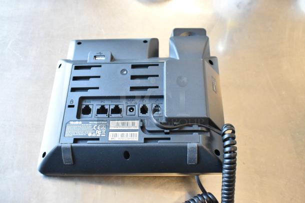 Yealink corded telephone with multiple ports visible on the back panel, model and certifications shown on labels.
