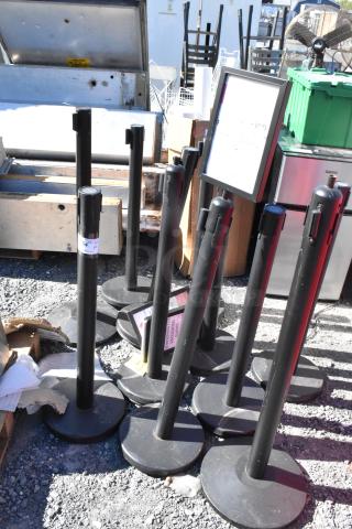10 QueueWay stanchions in used condition, black finish, solid bases, various labels attached; ideal for crowd control.