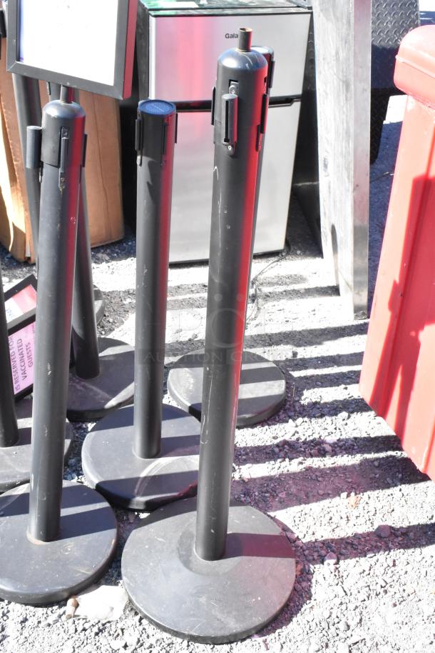 Set of 10 black QueueWay stanchions, used for crowd control. Sturdy bases, slight wear visible.