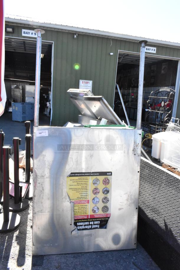 Stainless steel panel with visible wear and attached informational sticker, outdoors, in fair condition, industrial setting.
