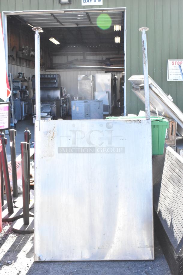 Stainless steel panel with visible rust and wear, rectangular, auctioned outdoors near warehouse bay.