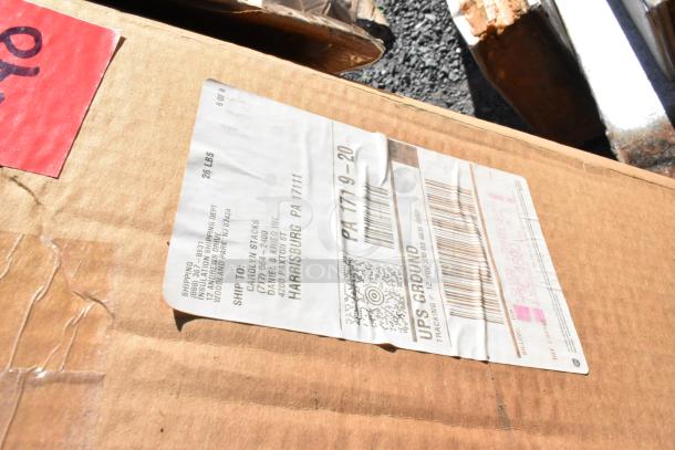 Cardboard box labeled for shipping, containing rolls of material. Shipping label shows a destination in Harrisburg, PA. Box is slightly worn.