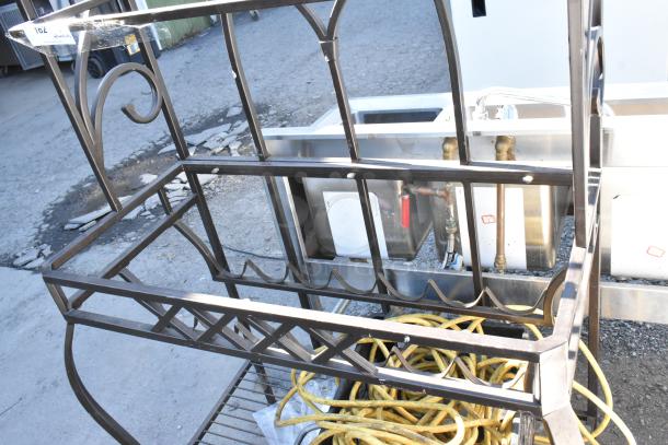 Metal frame with decorative scrollwork and integrated shelf, includes coiled yellow hose. Number tag "162" attached.