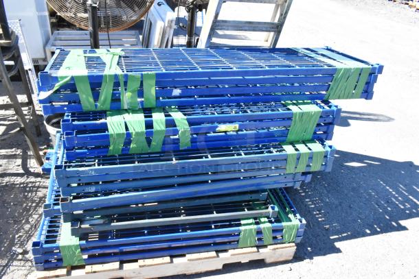 Lot of 18 blue metal wire shelves with poles, stacked and taped on a pallet. Suitable for storage solutions.