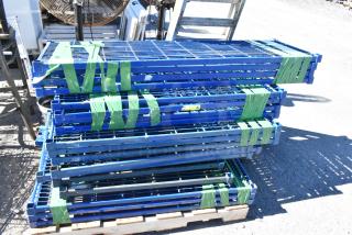 Lot of 18 blue metal wire shelves with poles, stacked and taped on a pallet. Suitable for storage solutions.