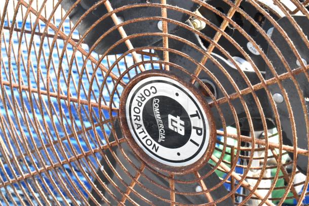 2 TPI FE-75S1fOL metal fans, floor style, 115V, 1 phase. Visible rust and TPI Corporation label in center grille.
