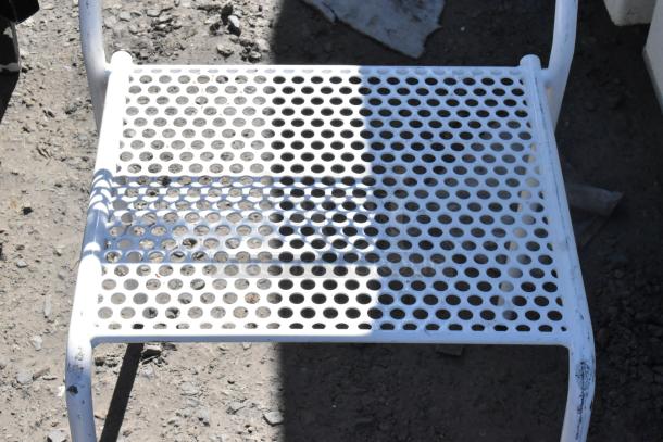 White perforated metal chair on a gravel surface, showing signs of wear. Part of an auction set of 5 various chairs.