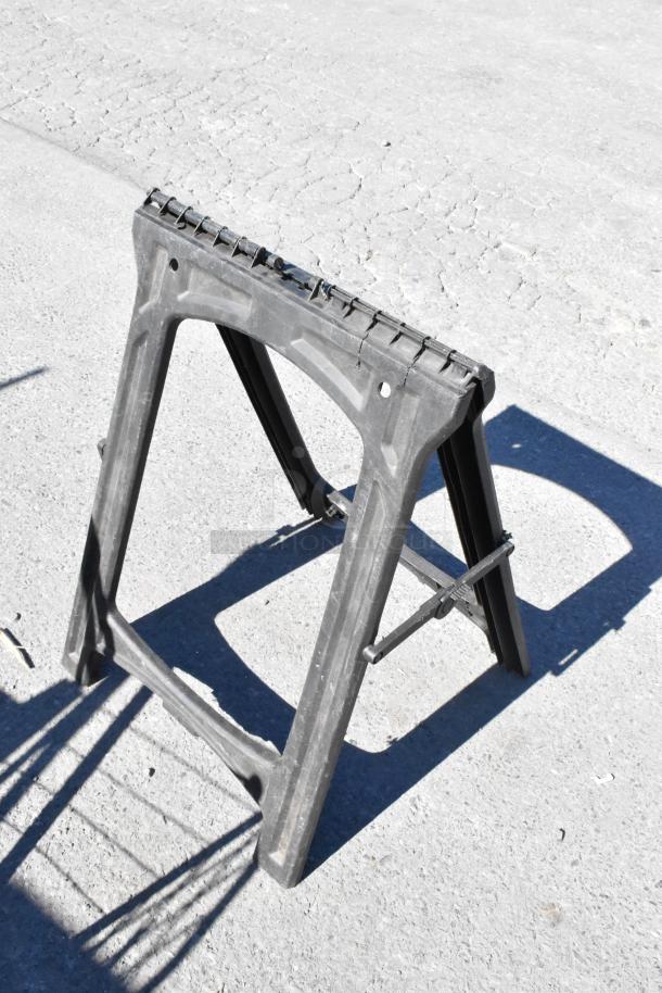 Auction item: Black plastic saw horse, sturdy and foldable, ideal for workshop use or construction support.