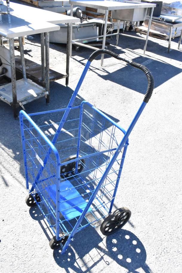 Blue folding utility cart with black handle and wheels, part of a lot including a folding table, sign, and saw horse.