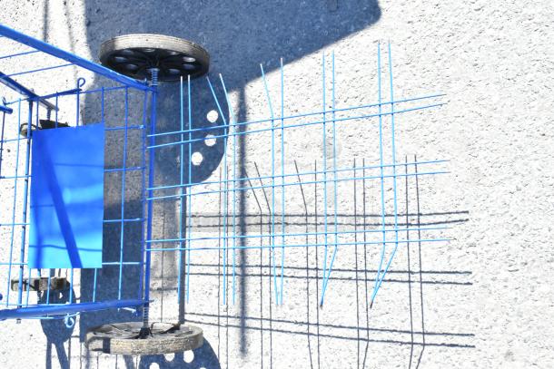 Four metal items including a folding table, sign, saw horse, and basket; blue, visible wheels, used condition.