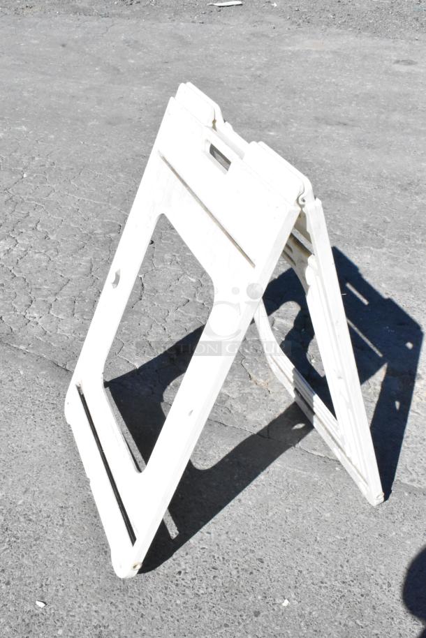 Folding white plastic sign on asphalt, portable and lightweight, good condition, suitable for advertising or directions.