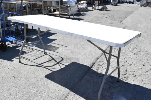 Folding table with metal legs on an outdoor surface, showing signs of wear.