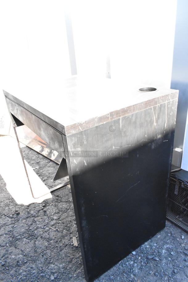 Black desk with a simple design, visible scratches and wear on the surface, includes a cable grommet.