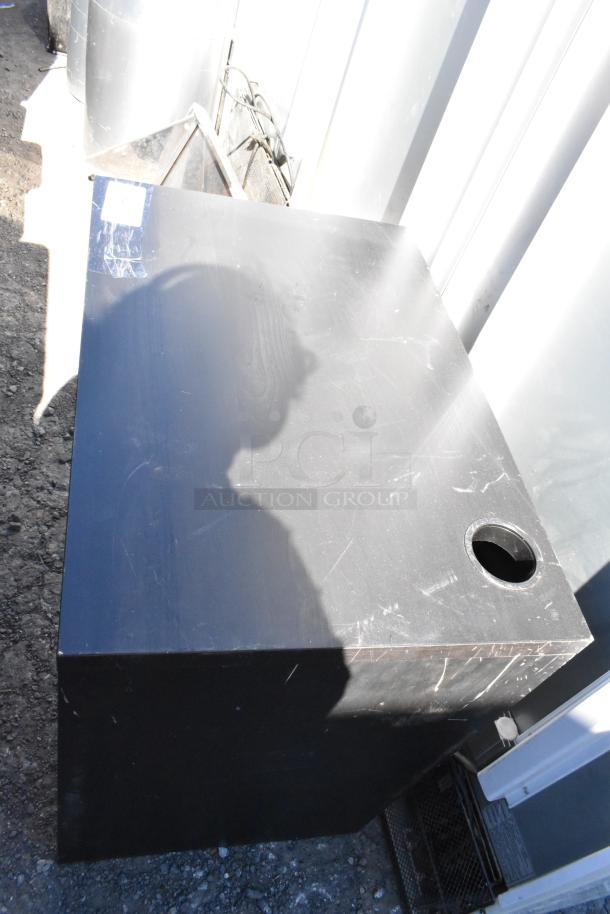 Black desk with cable hole, surface shows visible scratches and wear. Rectangular shape, no visible labels or markings.
