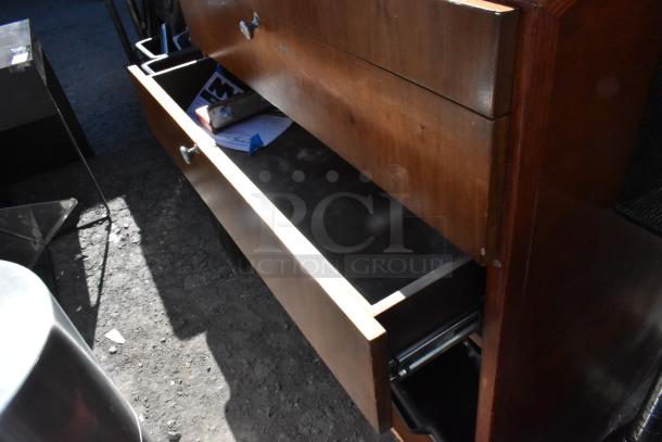 Wooden stand with two open drawers, displaying a rich brown finish and metal knobs. Visible signs of use; papers inside.