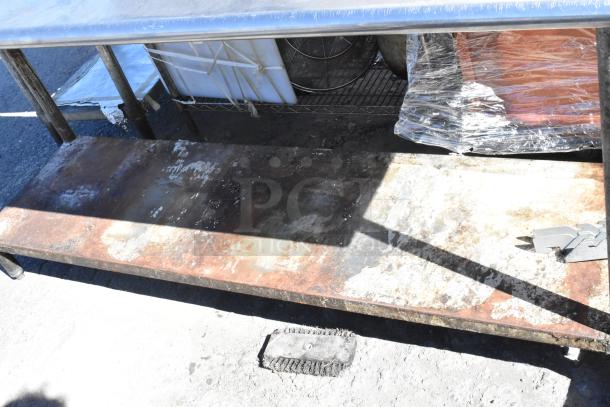 Stainless steel table with metal under shelf. Features robust design; shows signs of wear, ideal for industrial use.