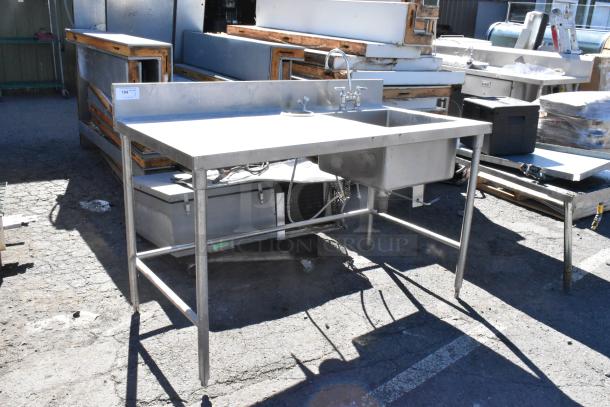 Stainless steel table with integrated sink basin, faucet, and handles. Features sturdy legs and durable construction. Ideal for kitchen use.