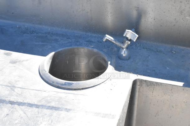 Stainless steel table with integrated sink basin, faucet, and handles. Visible wear and discoloration on the surface.